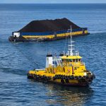 A yellow tugboat hauls a coal barge on calm waters in Indonesia, showcasing maritime industry.